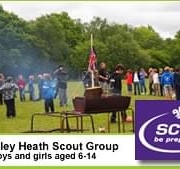 Children gather outdoors around a campfire at a scout event; “scouts be prepared” logo in corner.